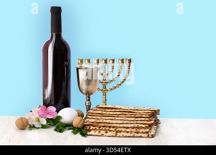 Matzo, Wein, Menora, Ei, Blumen Apfel, Nüsse für die pessach-Feier auf einem weißen Holztisch auf blauem Hintergrund mit Platz für Text Stockfoto