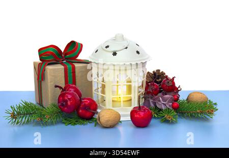 Weihnachtsdekoration. Weihnachtslaterne, Geschenkbox, rote Beeren, Pinienkegel, rote Äpfel, Nüsse, Weihnachtsbaum auf blauem Tisch auf weißem Hintergrund Stockfoto