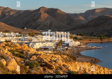 Golden Hour beleuchtet weiße Häuser im mediterranen Stil entlang einer ruhigen Bucht mit zerklüfteten Hügeln und einem Sandstrand. Costa Almeria, Spanien Stockfoto