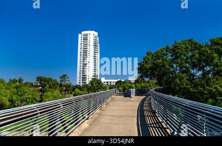 Rosemont Fußgängerbrücke in Houston, Texas, an einem sonnigen Tag. Die Brücke führt über den Buffalo Bayou Park mit einem Wohnhochhaus im Hintergrund Stockfoto
