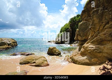 Goldener Sand und zerklüftete Felsen treffen auf die sanften Wellen eines türkisfarbenen Meeres unter einem Himmel voller flauschiger Wolken. Das ist Playa Teresa in Puerto Rico. Stockfoto