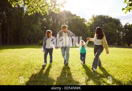 Vier Familienmitglieder, die an sonnigen Sommertagen Spaß im Park haben, gemeinsam spazieren gehen und Hände halten Stockfoto