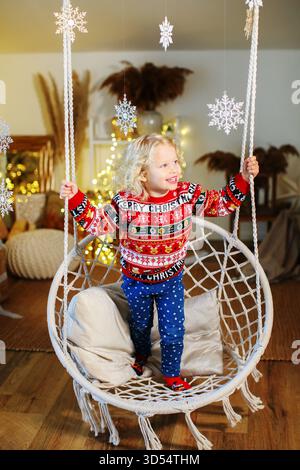 Kleines Mädchen in passenden Weihnachtspullover, das gemütliche Urlaubsmomente zu Hause mit festlicher Einrichtung genießt. Stockfoto