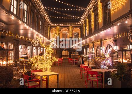 Wunderschön eingerichteter Innenhof in der Altstadt von Vilnius mit Weihnachtslichtern, festlichen Ornamenten und gemütlichen Sitzgelegenheiten im Freien unter warmem Lichterlicht Stockfoto
