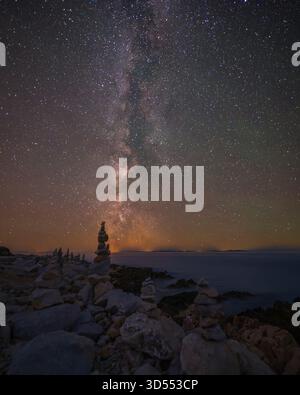 Rock formations stacked along a rugged shoreline under the glowing Milky Way core, captured at night with clear skies and bright celestial detail abov Stockfoto