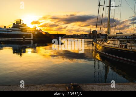 Sonnenuntergang glühen zwischen zwei großen Yachten im Yachthafen von Tarragona mit buntem Himmel, der sich in ruhigen mediterranen Gewässern spiegelt Stockfoto