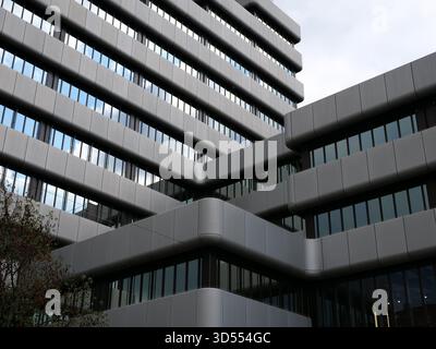Modernes Bürogebäude mit grauen Fassadenpaneelen und reflektierenden Glasfenstern. Architektonische Detailaufnahme, ideal für Stadtentwicklung, Business und Kontra Stockfoto