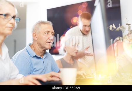 Geballter älterer Mann, der in der Bibliothek mit dem Computer eingetaucht ist Stockfoto