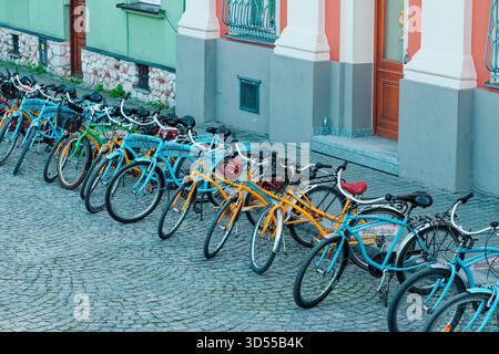 Eine Reihe farbenfroher Leihfahrräder parkt auf einer Kopfsteinpflasterstraße vor historischen Gebäuden. Stockfoto