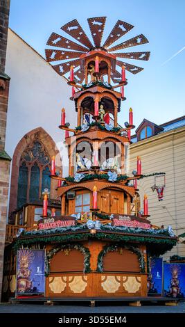 Basel, Schweiz - 16. November 2024: Große traditionelle hölzerne Weihnachtspyramide mit Krippenfiguren und roten Kerzen auf dem Weihnachtsmarkt Stockfoto