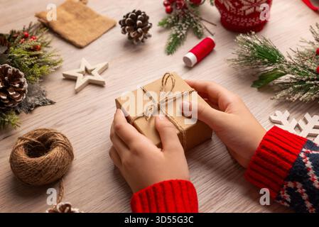 Nahaufnahme eines Kindes, das eine festliche Geschenkbox neben Weihnachtsdekorationen hält, ideal für detailfokussierte Weihnachtsbilder und saisonale Werbung Stockfoto