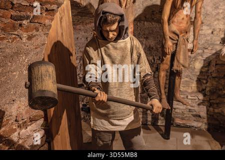 Transsilvanien, Rumänien - 8. Oktober 2025: Mittelalterliche Folterpuppe mit Kapuze, die einen Hammer in der dunklen Corvin Castle Folterkammer in Hunedoara hält Stockfoto