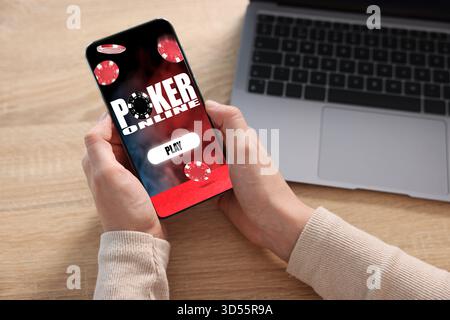 Frau spielt online Poker auf Handy an Holztisch, Nahaufnahme Stockfoto
