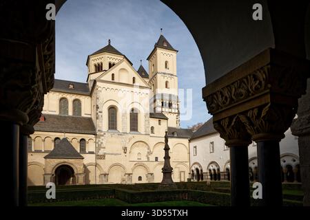 Ikonische Aussicht auf die romanische Abteikirche St. Nikolaus in Brauweiler, gerahmt von den dunklen Steinbögen des historischen Kreuzgangs und des Hofes Stockfoto