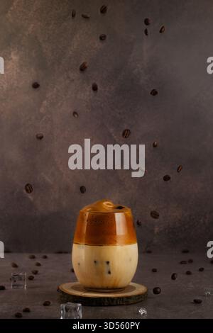 Ein mit Eismilch gefülltes Glas wird mit flauschigem Schlagkaffee getoppt und von Kaffeebohnen umgeben, die zu fallen scheinen. Die Einstellung ist einfach und Stockfoto