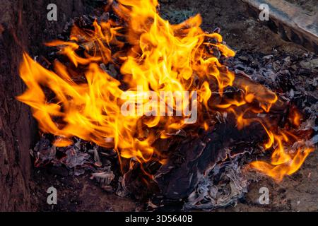 Ein kleines Feuer in einer provisorischen Grube am Boden verbrennt alte Dokumente mit hellen Flammen und viel fliegende Asche um sie herum. Selektiver Fokus Stockfoto
