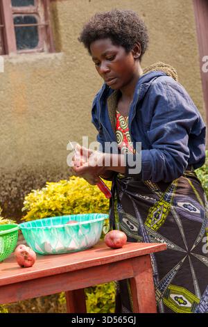 Gasura Ruanda - 8. September 2025; authentische afrikanische Dorffrau, die Kartoffeln für das Abendessen zubereitete und über Plastikschüssel schälte. Stockfoto