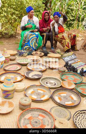 Gasura Ruanda - 8. September 2025; drei Frauen sitzen auf dem Boden und weben bunte Teller und Schüsseln, um sie an Touristen zu verkaufen. Stockfoto