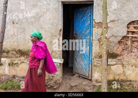 Gasura Ruanda - 8. September 2025; Afrikanerin in traditioneller, farbenfroher Kleidung mit rotem und rosa Rock und Umhang mit grünem Kopftuch, Walking aw Stockfoto