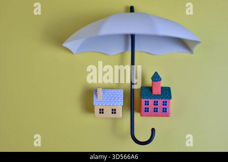 Große Regenschirme zwei Spielzeughäuser auf gelbem Hintergrund symbolisieren den Schutz, die Sicherheit und das Konzept der Versicherung. Stockfoto