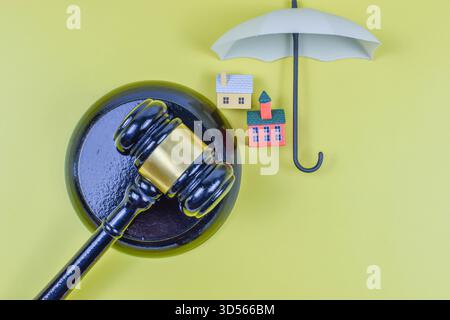 Der Hammer des Richters neben Modellhäusern auf gelbem Hintergrund symbolisiert die rechtliche Autorität in Eigentumsbesitz, Wohnungsstreitigkeiten oder Immobilienregulierung. Stockfoto