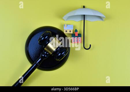 Der Hammer des Richters neben Modellhäusern auf gelbem Hintergrund symbolisiert die rechtliche Autorität in Eigentumsbesitz, Wohnungsstreitigkeiten oder Immobilienregulierung. Stockfoto