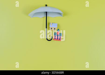 Große Regenschirme zwei Spielzeughäuser auf gelbem Hintergrund symbolisieren den Schutz, die Sicherheit und das Konzept der Versicherung. Stockfoto