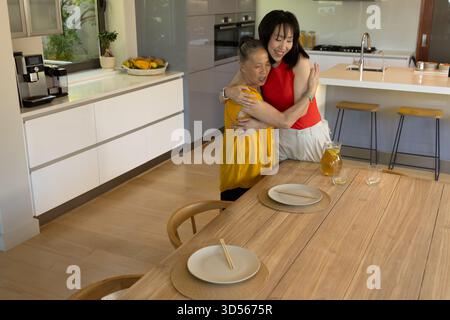 Seniorenmutter und Tochter, die sich in moderne Küche umarmen, gemeinsam einen freudigen Moment verbringen Stockfoto
