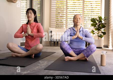 Zwei asiatische Frauen üben zu Hause Yoga-Meditation, sitzen im Kreuz auf Matten. Achtsamkeit, Wellness, Bewegung, Ruhe, Fitness, ruhig Stockfoto