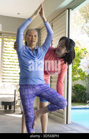 Asiatisch-chinesische Trainerin und Kundin üben Yoga auf gefliester Terrasse mit Pool-Hintergrund Stockfoto