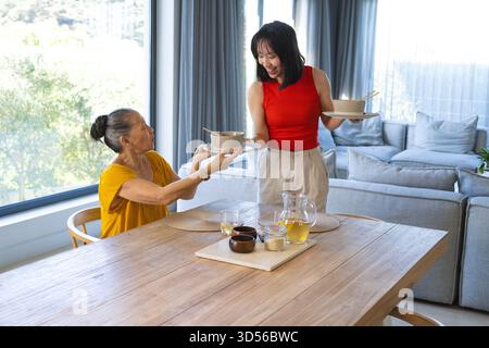 Vorbei an asiatisch-chinesischen Mutter und Tochter, die am Esstisch Schüsseln austauschen, mit Tee-Set Stockfoto