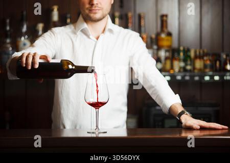Sommeliermännchen gießt Rotwein in langstielige Weingläser. Stockfoto