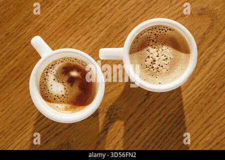Zwei weiße Tassen Cappuccino mit reichhaltigem Schaum auf Holztisch, Blick von oben Stockfoto