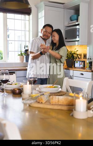 Reifes Paar tanzt in der Küche und genießt romantische Momente mit Wein und Kerzen Stockfoto