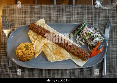 Shish Kabab mit Hackfleisch auf Fladenbrot. Traditionelle köstliche türkische Gerichte, Adana-Kebab serviert mit Zwiebelsalat, gegrillten Tomaten und grünem Pfeffer Stockfoto