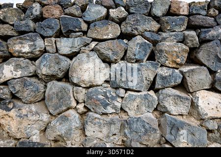 Eine Mauer aus großen Felsen. Die Wand ist grau und hat eine raue Textur. Die Felsen haben verschiedene Größen und Formen und sind auf jedem der Felsen gestapelt Stockfoto
