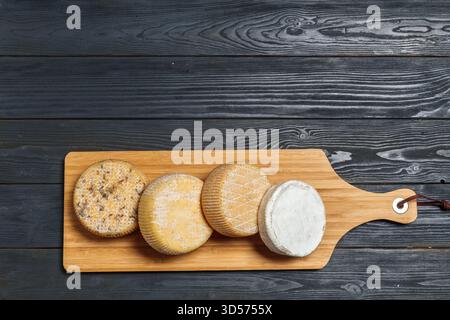 Verschiedene Käsesorten werden auf einem Holzbrett in einer einfachen Kücheneinrichtung präsentiert Stockfoto