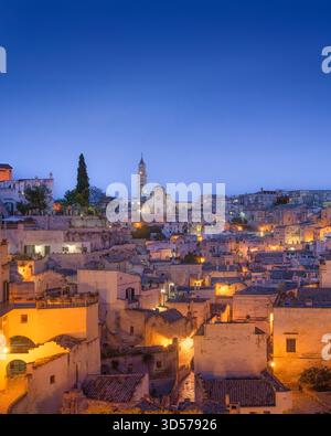 Vertikale Aufnahme der Sassi di Matera in der Dämmerung, blaue Stunde. Die alten Höhlenhäuser und Gebäude leuchten mit warmem Licht mit der Kathedrale Stockfoto
