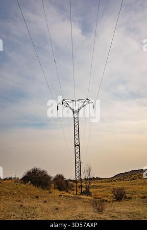Ein hoher Stromleitungsturm steht auf einem Feld. Der Himmel ist bewölkt und die Sonne ist niedrig am Himmel Stockfoto