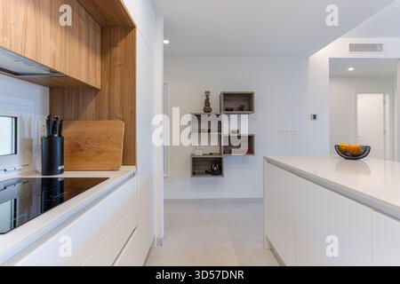 Eleganter Küchenbereich mit weißen Schränken, Holzpaneelen, modernen Geräten und stilvollen offenen Regalen an neutralen Wänden. Stockfoto