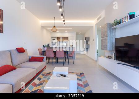 Moderner Wohnbereich mit gemütlichen Sitzgelegenheiten, Esstisch und Küche mit Holzakzenten in heller, offener mediterraner Einrichtung. Stockfoto