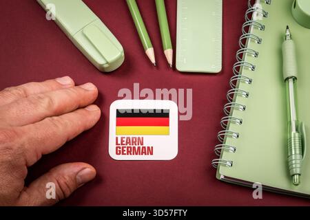 Hand neben, um Deutsch zu lernen Karte mit Deutschland Flagge umgeben von Briefpapier und Notizbuch, Konzept des Studiums Fremdsprache und Bildung. Stockfoto