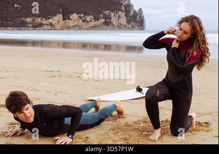 Mann und Frau in Neoprenanzügen bereiten sich vor und dehnen sich, bevor sie ins Meer gehen, um zu surfen Stockfoto