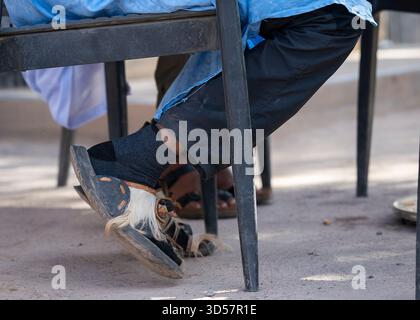 Traditionelle marokkanische Sandalen mit Haarklemmen, die unter einem Tisch im Freien getragen werden. Nahaufnahme handgefertigter Ledersandalen. Stockfoto