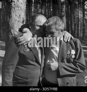 Dieses archivierte Schwarzweißfoto aus dem Jahr 1985 zeigt ein zutiefst emotionales „Treffen der Freunde“ in Swiatohirsk (Slavyanogorsk), ukrainische SSR, anlässlich des 40. Jahrestages des Siegtages (9. Mai). In einem sonnendurchfluteten Kiefernwald teilen sich zwei ältere Veteranen des Zweiten Weltkriegs, deren Anzüge mit Medaillen verziert sind, eine kraftvolle, herzliche Umarmung. Ein Veteran hat seine Arme um seinen Kameraden gewickelt, sein Gesicht ist voller überwältigender Emotionen – vielleicht Tränen, Lieder oder ein Erinnerungsschrei. Dies ist ein tiefgreifender, ehrlicher Moment der Kameradschaft und der gemeinsamen Geschichte. Stockfoto