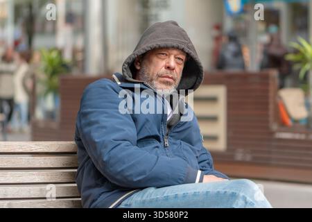 Ein Mann in warmen Kleidern sitzt auf einer Bank in einer Stadtstraße. Stockfoto