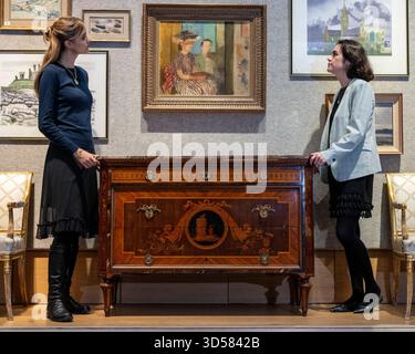 London, Großbritannien. 14. November 2025. Mitarbeiter mit „eine außergewöhnliche langobardische Kommode des frühen 19. Jahrhunderts“ von Giuseppe Maggiolini, ca. 1805-1810, (Schätzung £ 50.000 - £ 80.000) unter Victor Pasmore R.A. (britisch, 1908-1998) „The Painting Lektion“, 1939, (Schätzung £ 30.000 - £ 50.000) bei einer Vorschau auf den Verkauf von Lady Glenconner, My Life in Objects in Bonhams. Lady Glenconner war Maid of Honour bei der Krönung von Königin Elisabeth II. 1953 und Lady in Warten auf ihre Jugendfreundin Prinzessin Margaret. Die Lose werden am 18. November in den Bonhams New Bond Street Galerien versteigert. Quelle: Stephen Chung Stockfoto