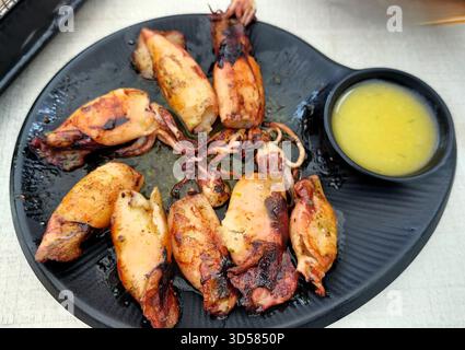 Gegrilltes Baby Calamari serviert mit Zitronensauce auf schwarzem Teller Stockfoto