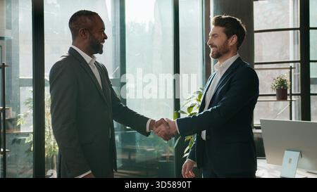 Zwei multiethnische Männer Geschäftsleute Geschäftsteam in Firmensitzung Begrüßung Handschütteln Gespräch diverser kaukasischer Geschäftsmann Stockfoto
