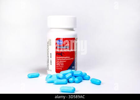 Weiße Flasche Kroger Acetaminophen PM-Kapseln mit rotem Etikett, umgeben von verstreuten blauen Pillen auf weißem Hintergrund Stockfoto